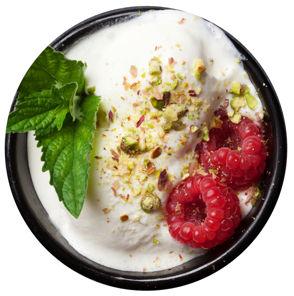 Vanilla ice cream in a bowl with pistachios, mint leaves and raspberries on top